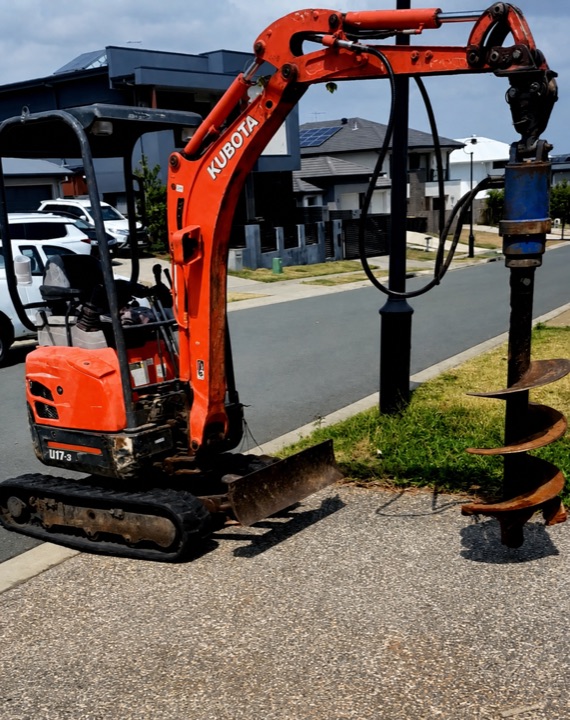 Compact Kubota excavator fitted with an auger beside a suburban street