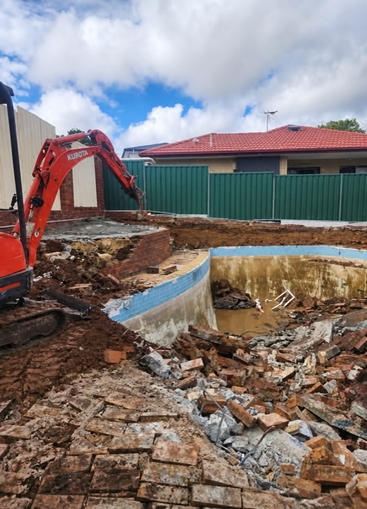 Mini excavator clearing brick and concrete around an old swimming pool